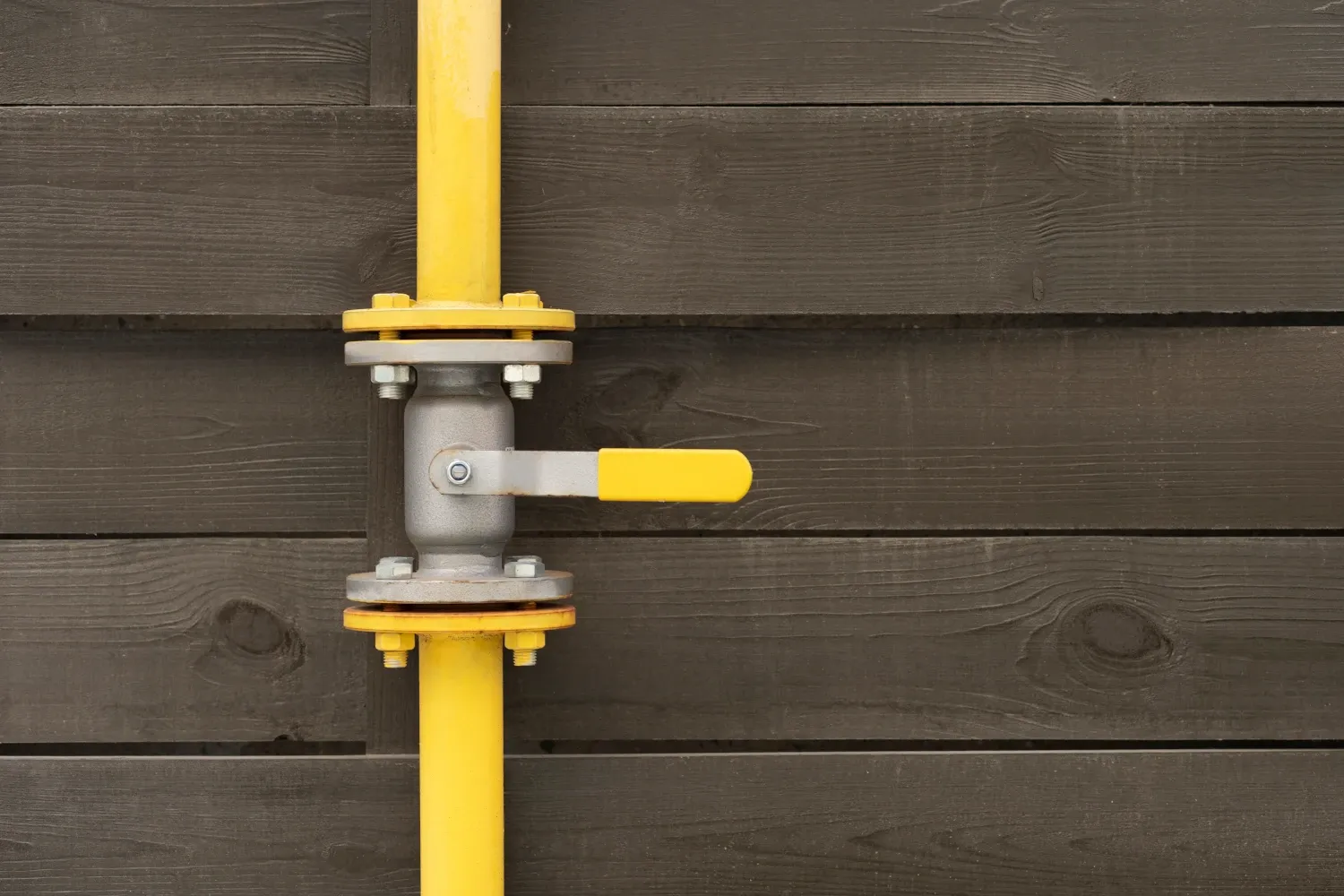Válvula de gas con tubería amarilla instalada en una pared de madera oscura. Mantener en óptimas condiciones las válvulas y tuberías es crucial para la seguridad y eficiencia en el suministro de gas. NetJet ofrece inspección y mantenimiento profesional.